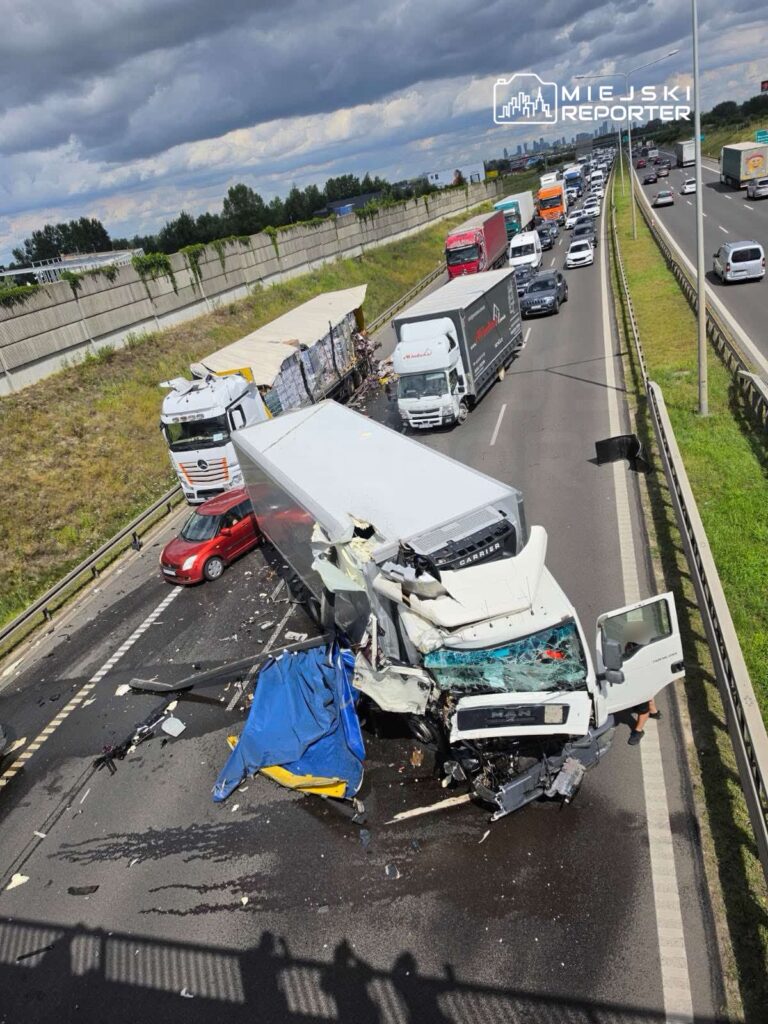 Zderzenie ciężarówki z osobówką na autostradzie, wokół rozrzucone fragmenty pojazdów i zablokowany ruch.