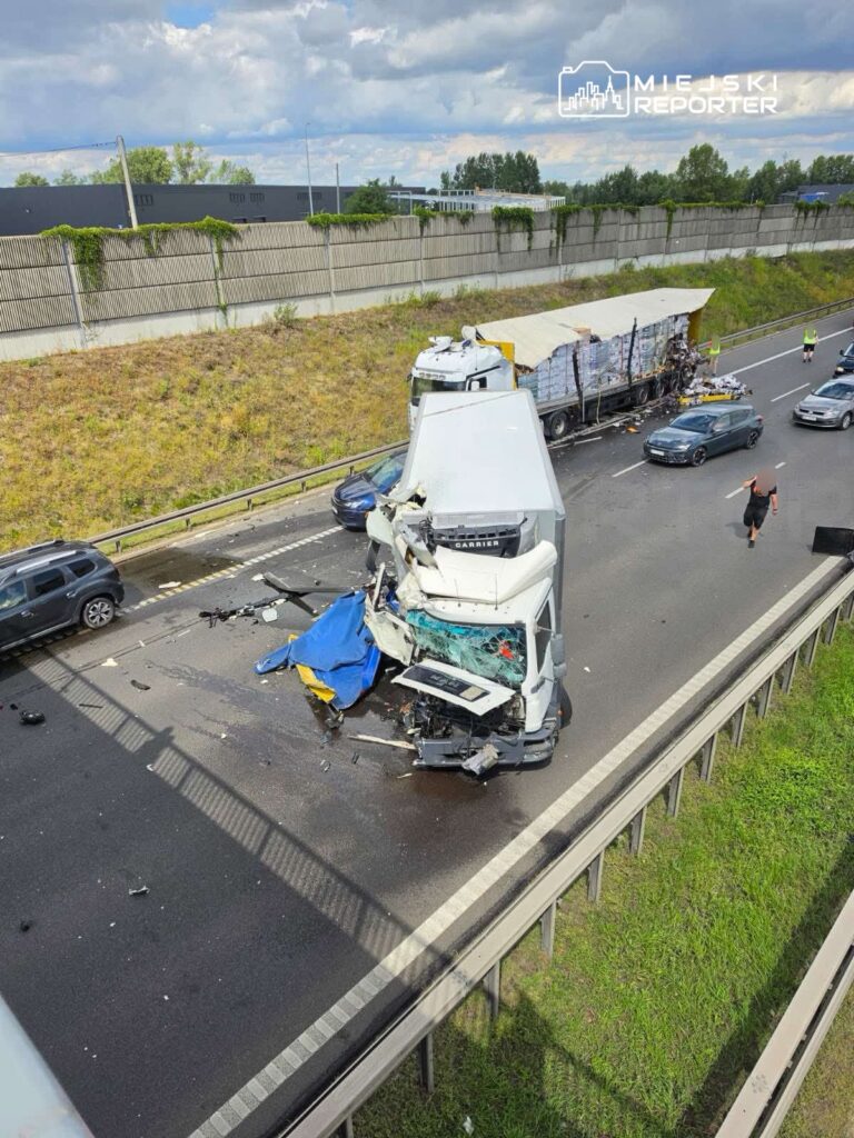 Zderzenie dwóch pojazdów na autostradzie, z uszkodzonym ciężarowym samochodem i rozrzuconymi elementami na jezdni.