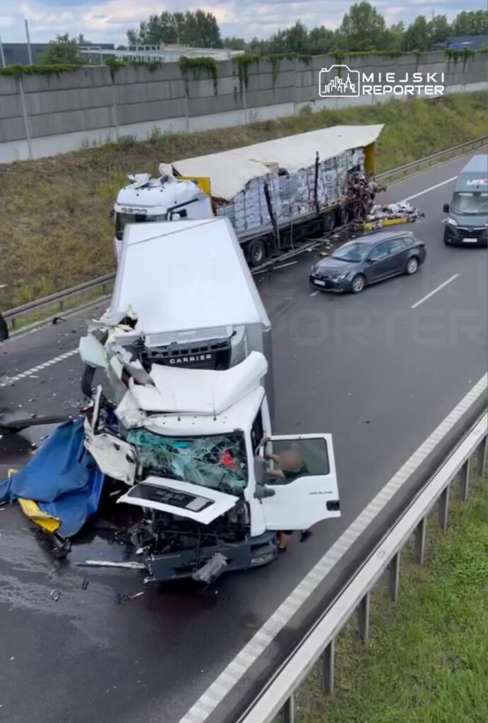 Zniszczona ciężarówka z rozbitą kabiną stoi na pasie ruchu, obok poruszające się samochody osobowe.
