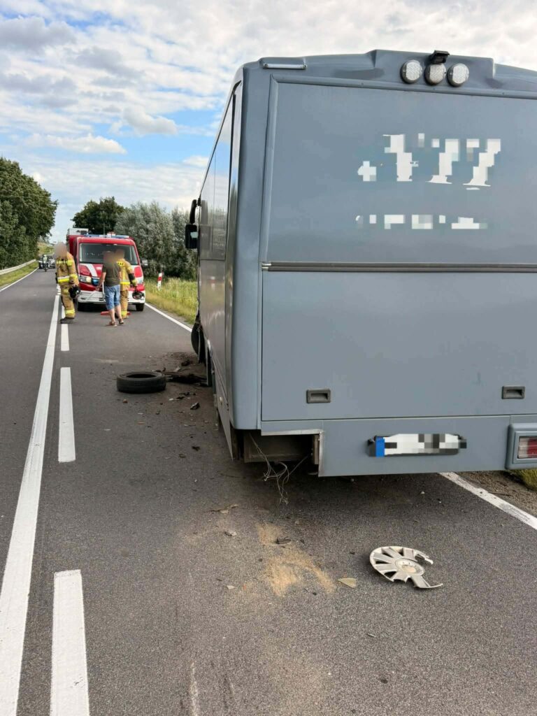 Uszkodzony autobus stoi na drodze, obok pracują strażacy oraz zespół ratunkowy. W tle widoczna zieleń.