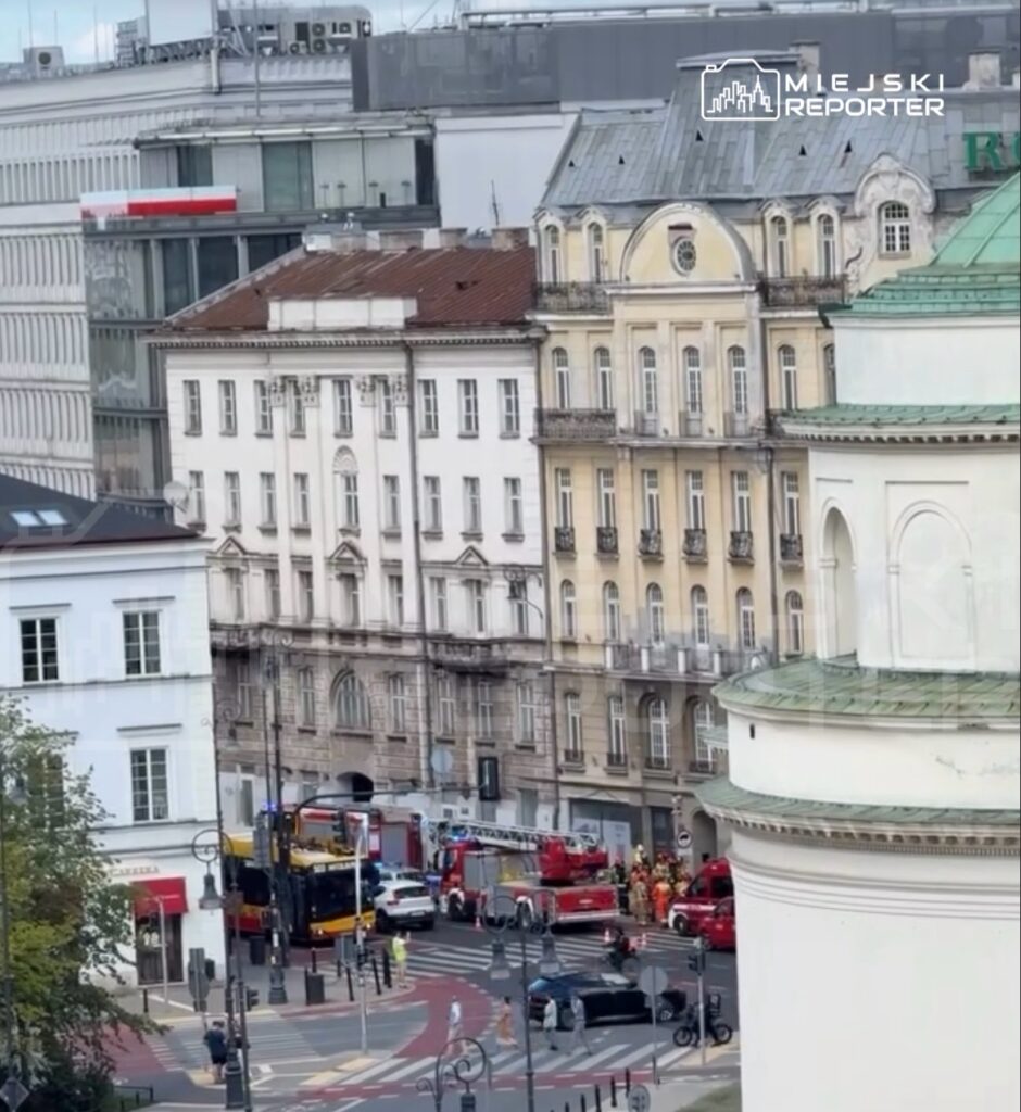 W centrum miasta zespół strażaków pracuje przy wozach strażackich na ruchliwej ulicy.