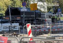Samochód patrolowy oraz ciężarówka z napisem "PATROL SAPERSKI" na ruchliwej ulicy, otoczone barierkami budowlanymi.