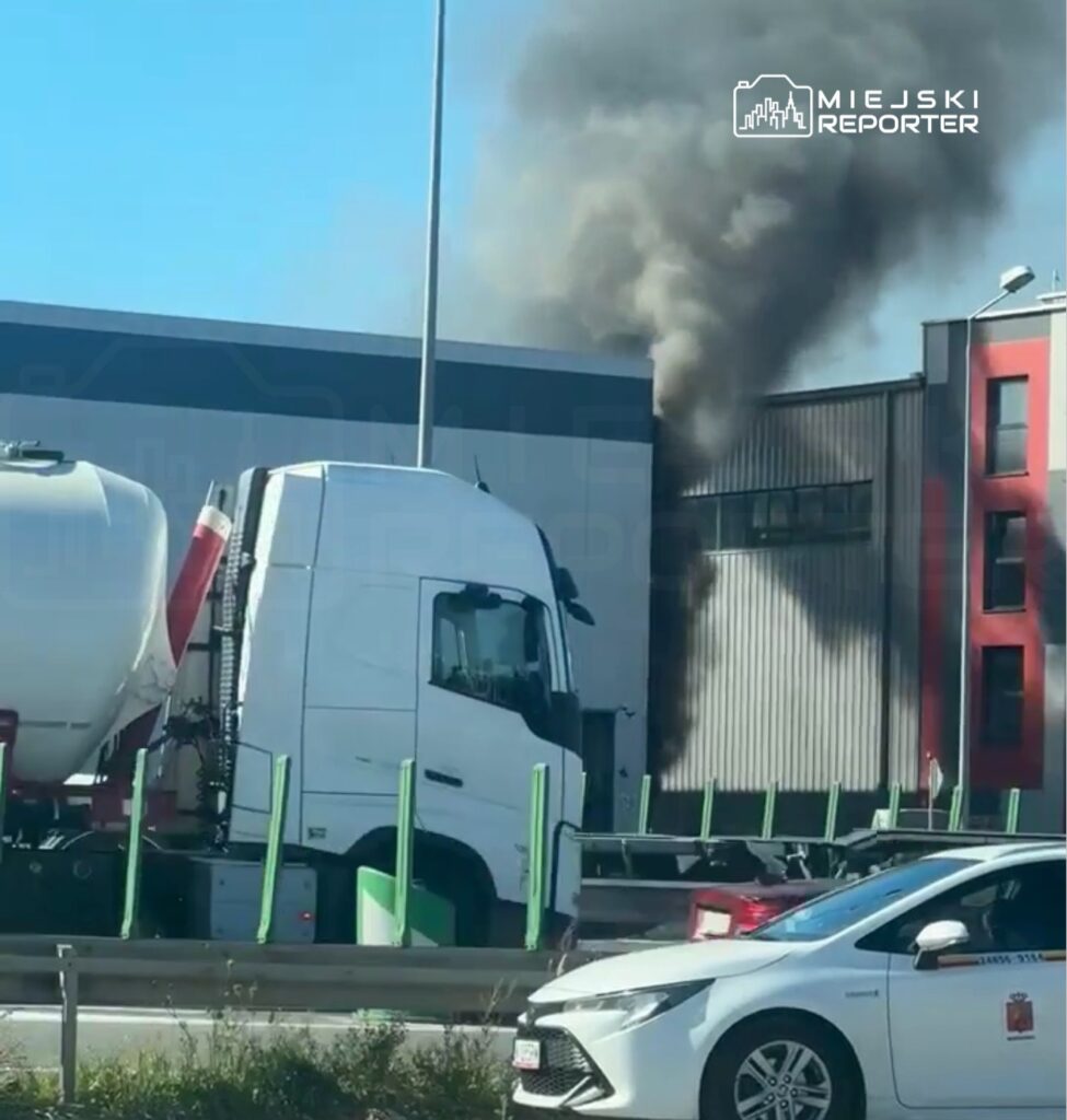 Czarny dym wydobywający się z budynku obok drogi, obok ciężarówki i osobowego samochodu.