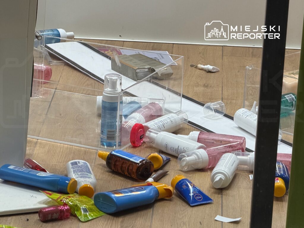 Rozrzucone kosmetyki, w tym butelki i tubki, leżą na podłodze w pomieszczeniu z drewnianą podłogą.