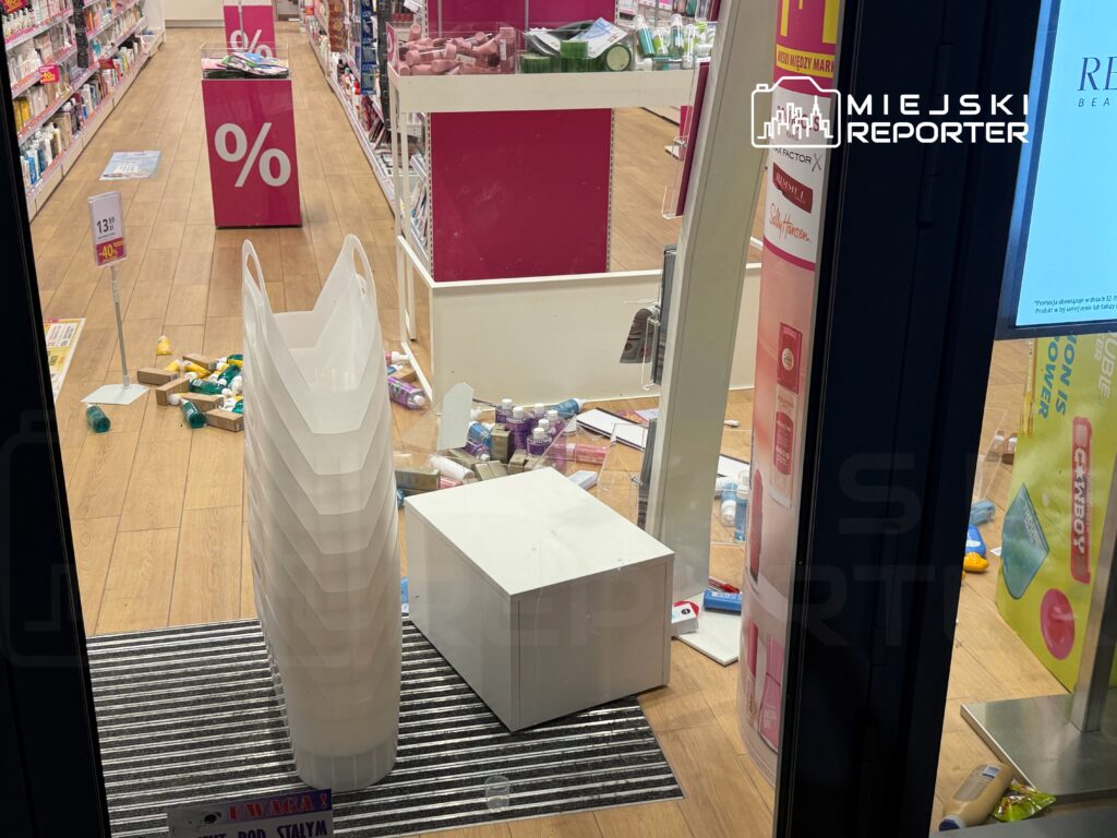 Rozrzucone produkty kosmetyczne na podłodze w sklepie, obok stos plastikowych pojemników i biały stolik.