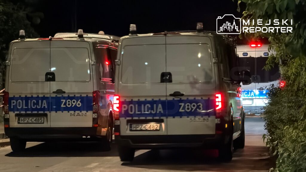 Dwa radiowozy policyjne zaparkowane na ulicy w nocy, z widocznymi numerami identyfikacyjnymi.