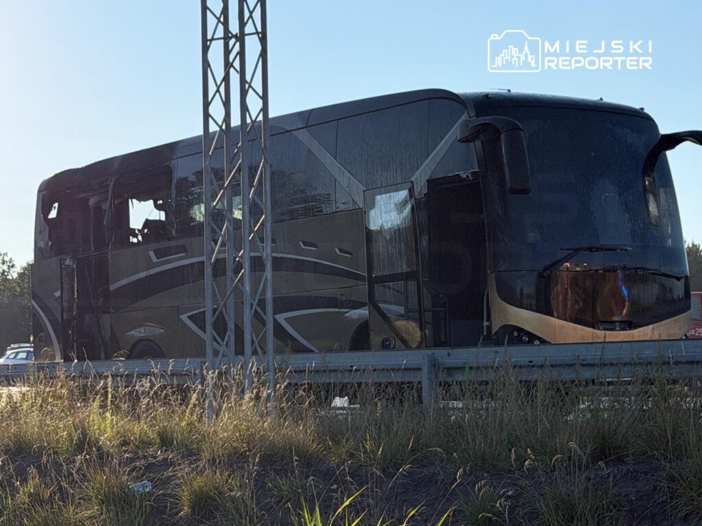 Autobus z uszkodzoną częścią nadwozia stoi na poboczu drogi, otoczony wysoką trawą.