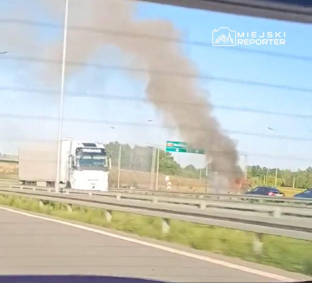 Na autostradzie widoczny dym wydobywający się z płonącego pojazdu obok ciężarówki.