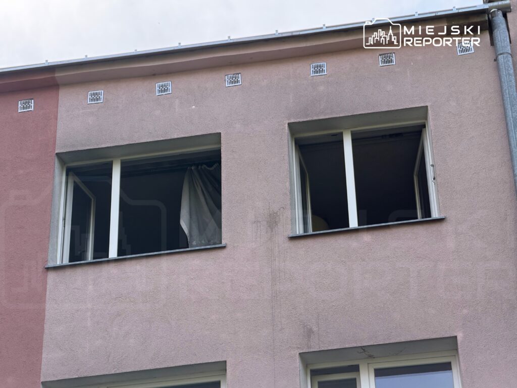 Dwa otwarte okna w różowym budynku, z białą firanką widoczną w jednym z nich.