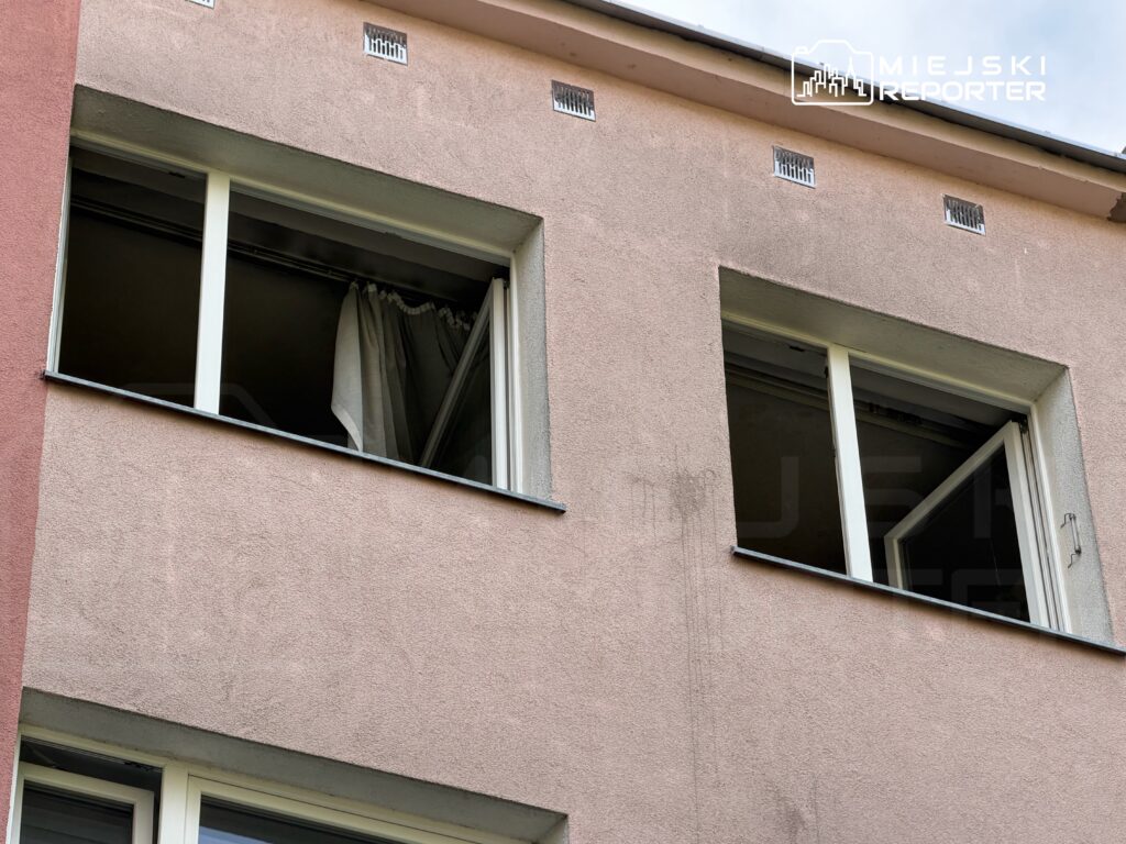 Okno w elewacji budynku z różową ścianą, z zasłoną w środku, lekko otwarte.
