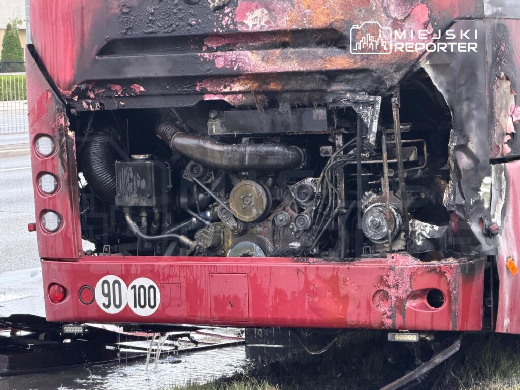 Spalona tylna część czerwonego autobusu miejskiego, odsłaniająca uszkodzony silnik oraz przewody.