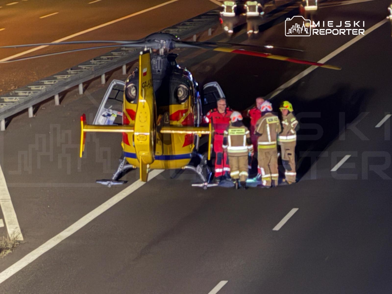 Ratownicy medyczni i strażacy współpracują przy śmigłowcu ratunkowym na autostradzie w nocy.