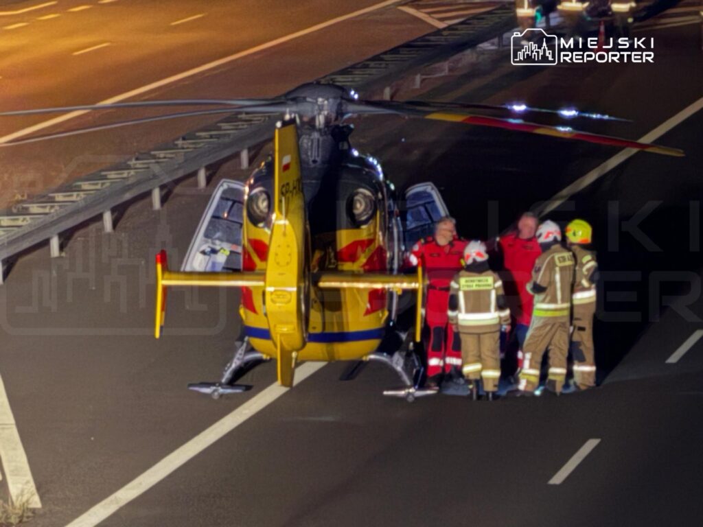 Zespół ratunkowy w czerwonych strojach omawia sytuację obok śmigłowca na autostradzie.