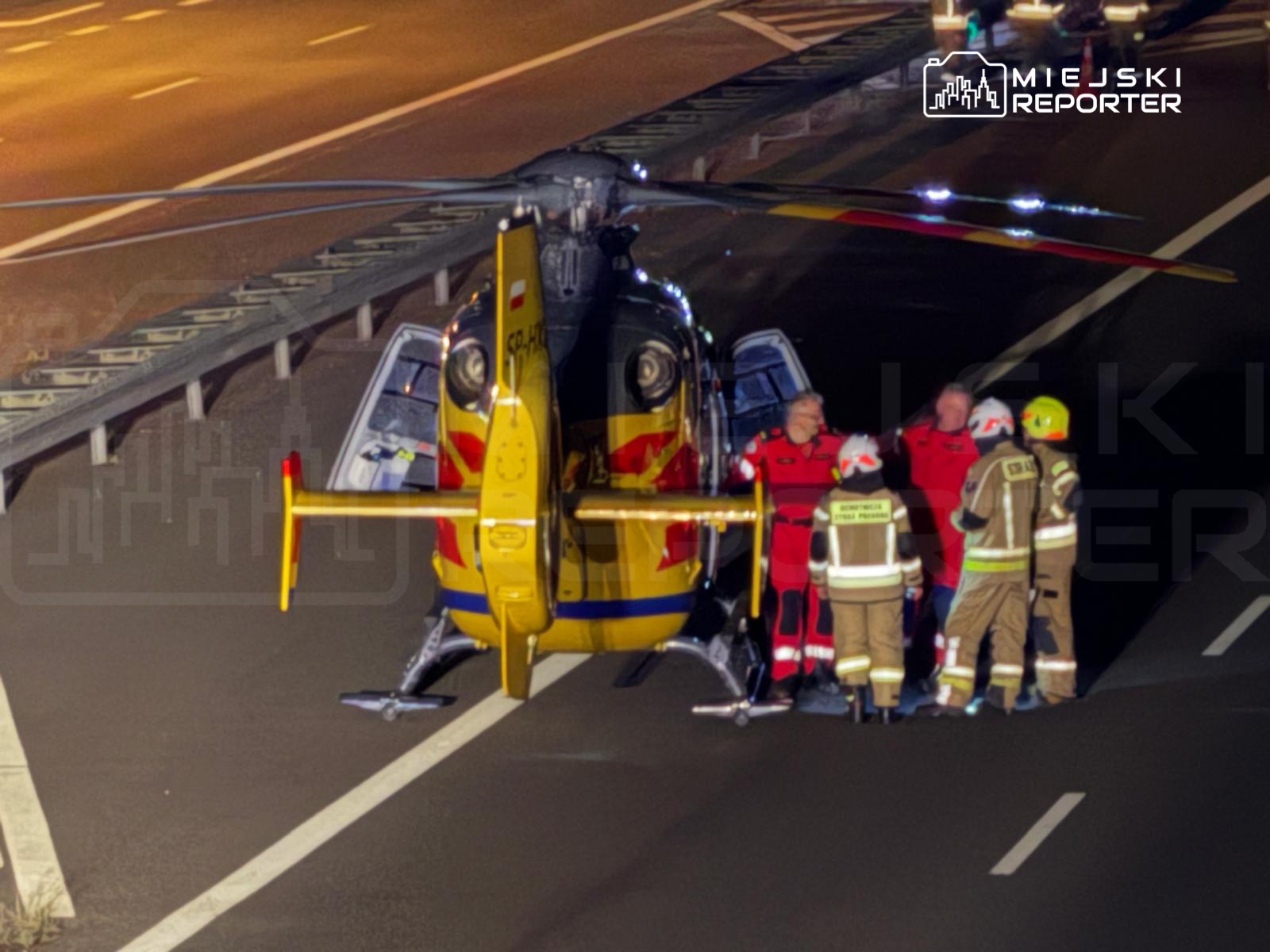 Zespół ratunkowy w czerwonych strojach omawia sytuację obok śmigłowca na autostradzie.