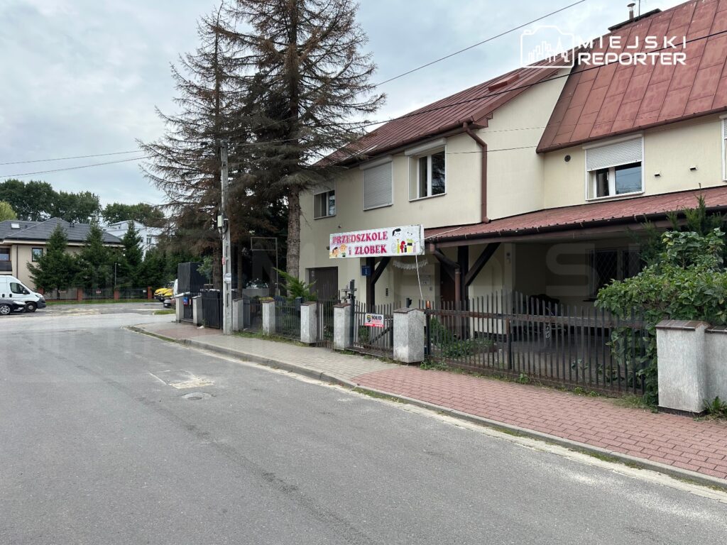 Przedszkole z kolorowym szyldem „Przedszkole z Złobek” znajdujące się w budynku z jasną elewacją, otoczone drzewami.