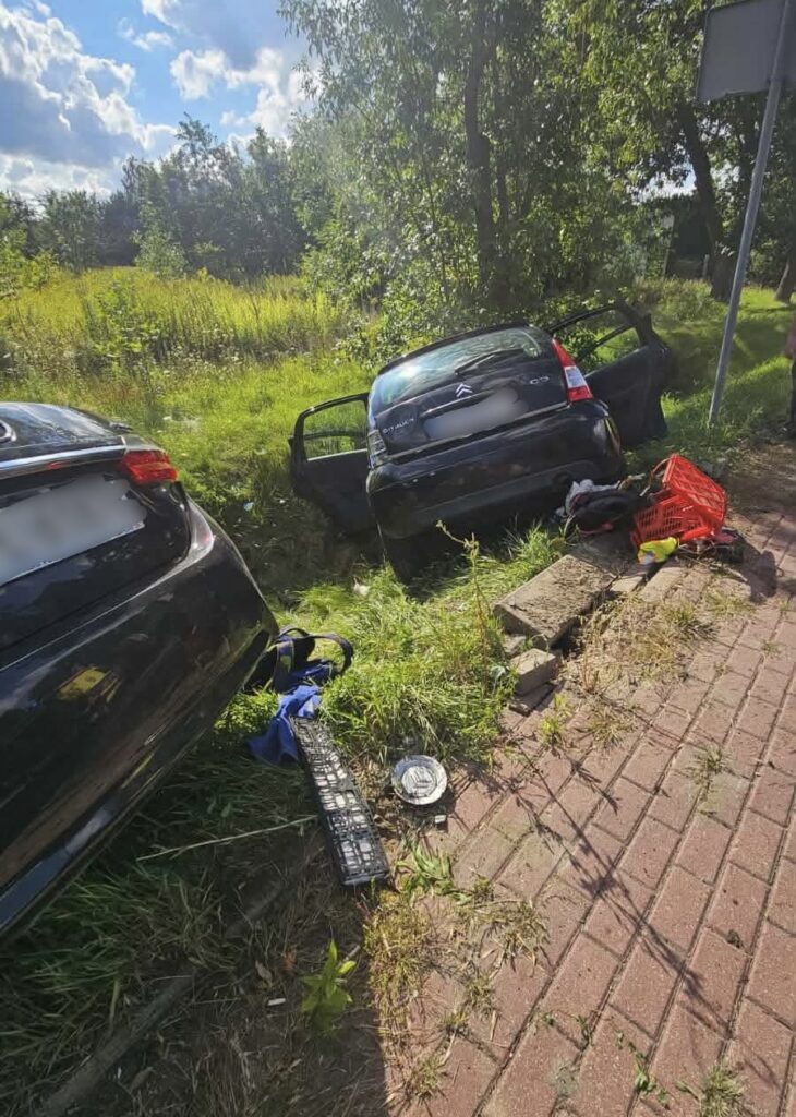 Czarny samochód osobowy zaparkowany na poboczu drogi, z otwartymi drzwiami, w otoczeniu trawy i drzew.
