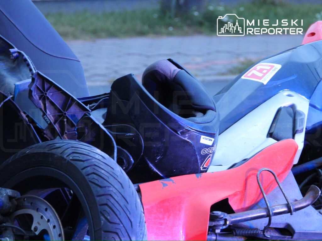 Czarna kask motocyklowy leży obok czerwonej i niebieskiej motocykla na chodniku.