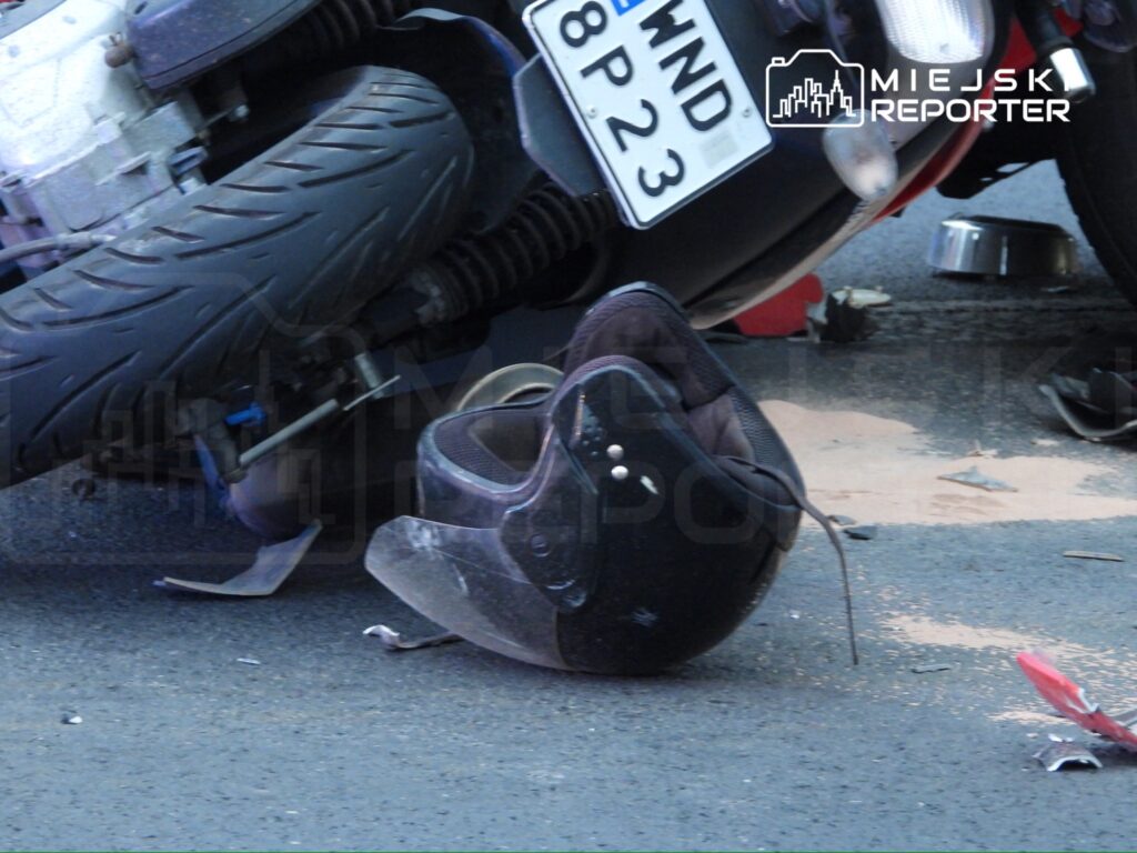 Przewrócony motocykl leży na jezdni obok czarnego kasku, a wokół rozsypane drobne elementy.