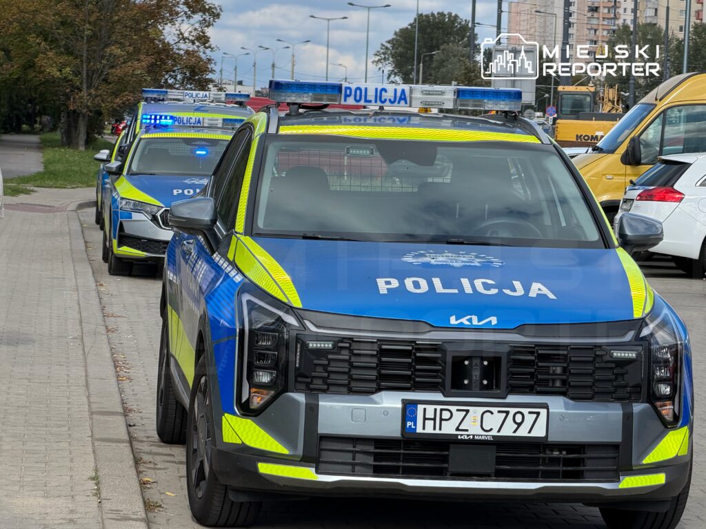 Trzy radiowozy policyjne zaparkowane na ulicy, z włączonymi sygnałami świetlnymi.