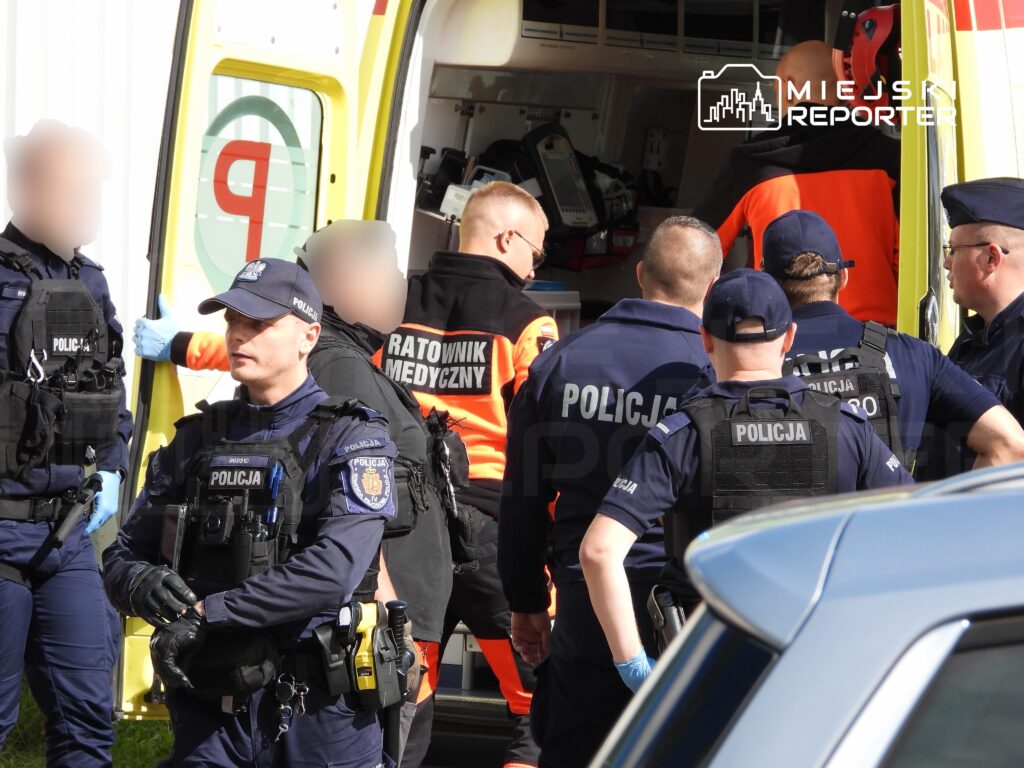 Grupa policjantów i ratowników medycznych współpracuje przy ambulansie, przygotowując się do akcji ratunkowej.