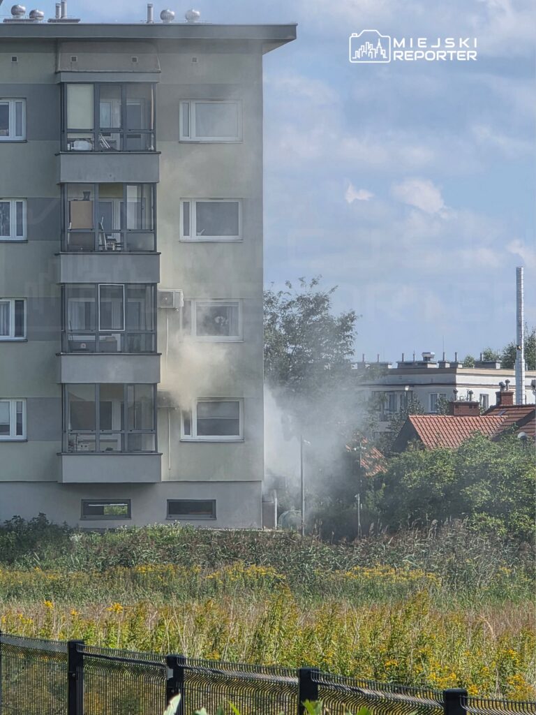 Wydobywający się dym z okna mieszkania na trzecim piętrze nowoczesnego budynku mieszkalnego.