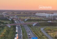 Wielka kolizja drogowa z udziałem kilku pojazdów na autostradzie, w tle widoczne samochody stojące w korku.