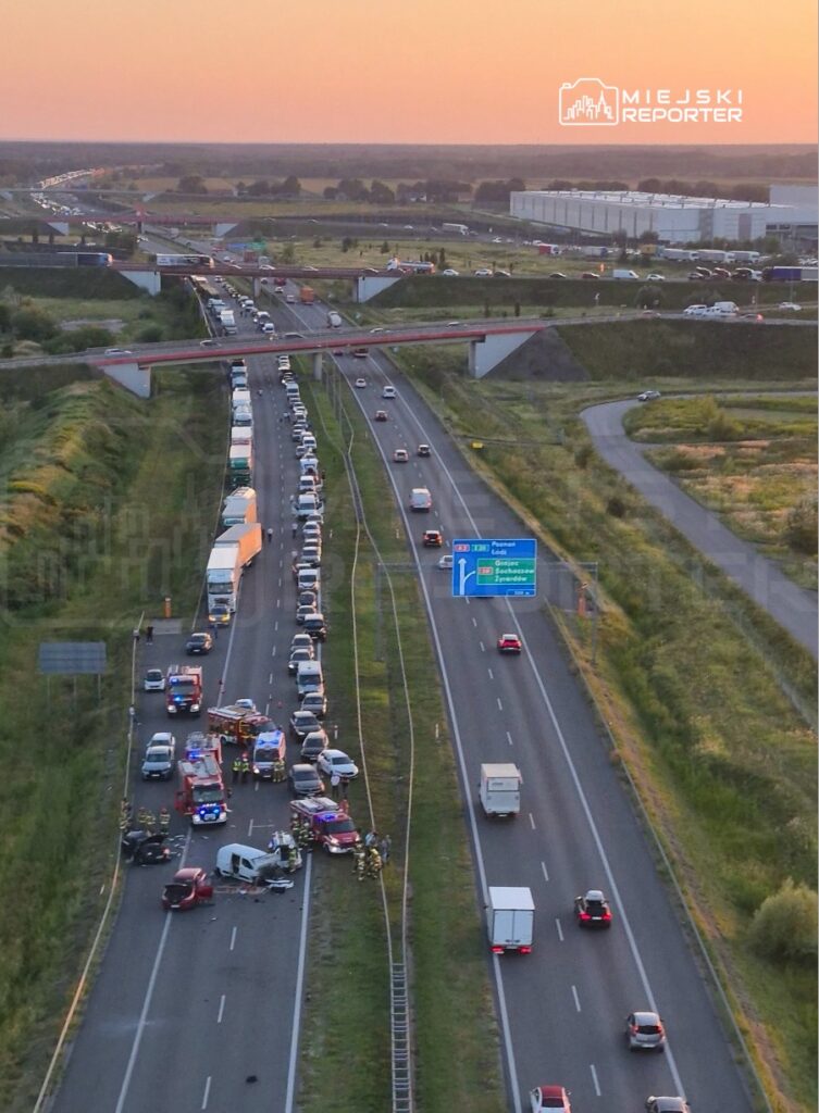 Wielka kolizja drogowa z udziałem kilku pojazdów na autostradzie, w tle widoczne samochody stojące w korku.