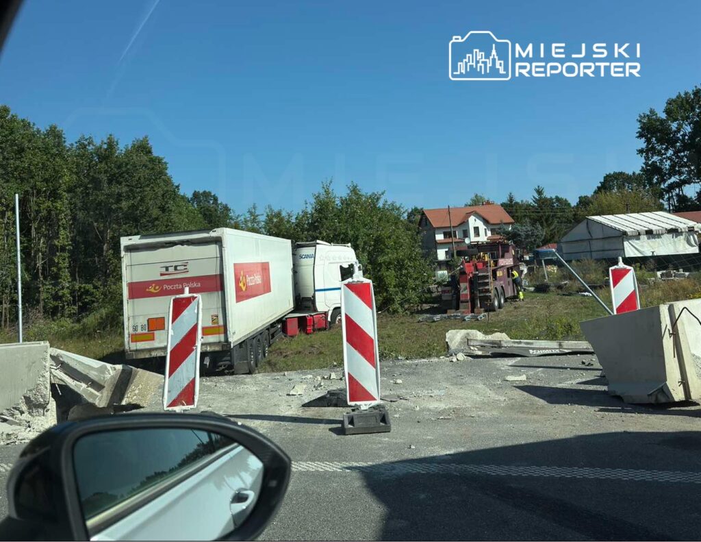 Ciężarówka z logo Poczty Polskiej stoi przy barierkach drogi, obok trwają prace drogowe z użyciem dźwigu.