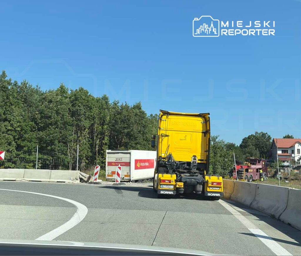 Żółta ciężarówka Scania zjeżdża z drogi w kierunku prac budowlanych, obok niej stoi inny pojazd dostawczy.