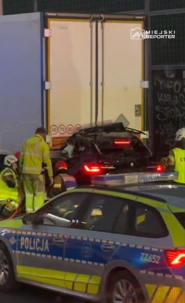 Ratownicy medyczni pracują przy uszkodzonym samochodzie, który zderzył się z ciężarówką w miejskiej okolicy.