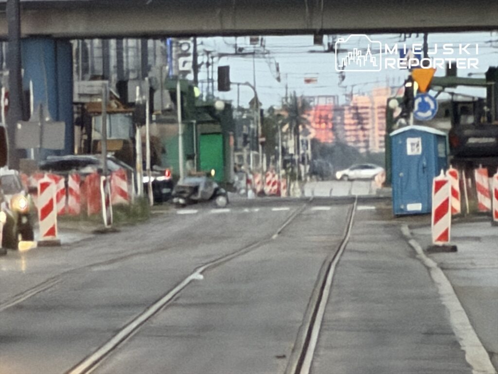 Zabudowane torowisko tramwajowe z oznakowaniami drogowymi i sprzętem budowlanym w miejskim otoczeniu.