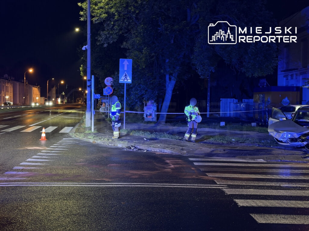 Policjanci w odblaskowych kamizelkach zabezpieczają miejsce wypadku drogowego nocą na ulicy z widoczną uszkodzoną furgonetką.