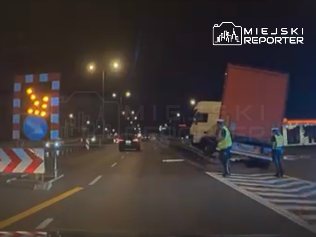 Dwaj mężczyźni w kamizelkach odblaskowych kierują ruchem na drodze, gdzie stoi uniesiony samochód ciężarowy.