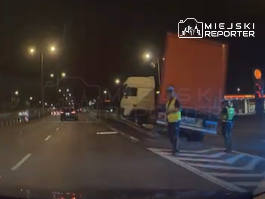 Dwaj mężczyźni w kamizelkach odblaskowych kierują ruchem na drodze, obok stoi ciężarówka.