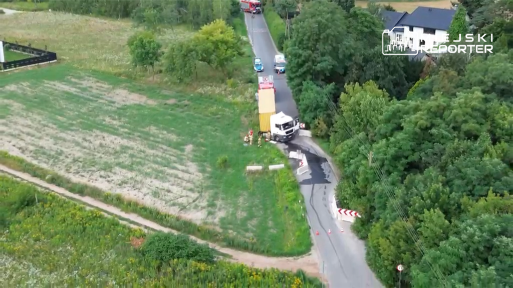 Ciężarówka zablokowana na drodze, obok strażacy zabezpieczają miejsce zdarzenia w otoczeniu zieleni.