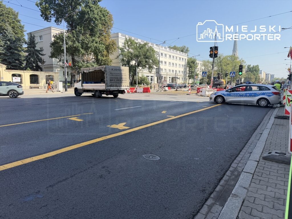 Ruch uliczny na zamkniętej Aleji „Solidarności” w Warszawie, z policyjnym radiowozem i ciężarówką.
