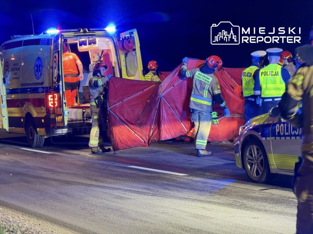 Ratownicy medyczni i strażacy ustawiają czerwony namiot na jezdni, podczas akcji ratunkowej w nocy.
