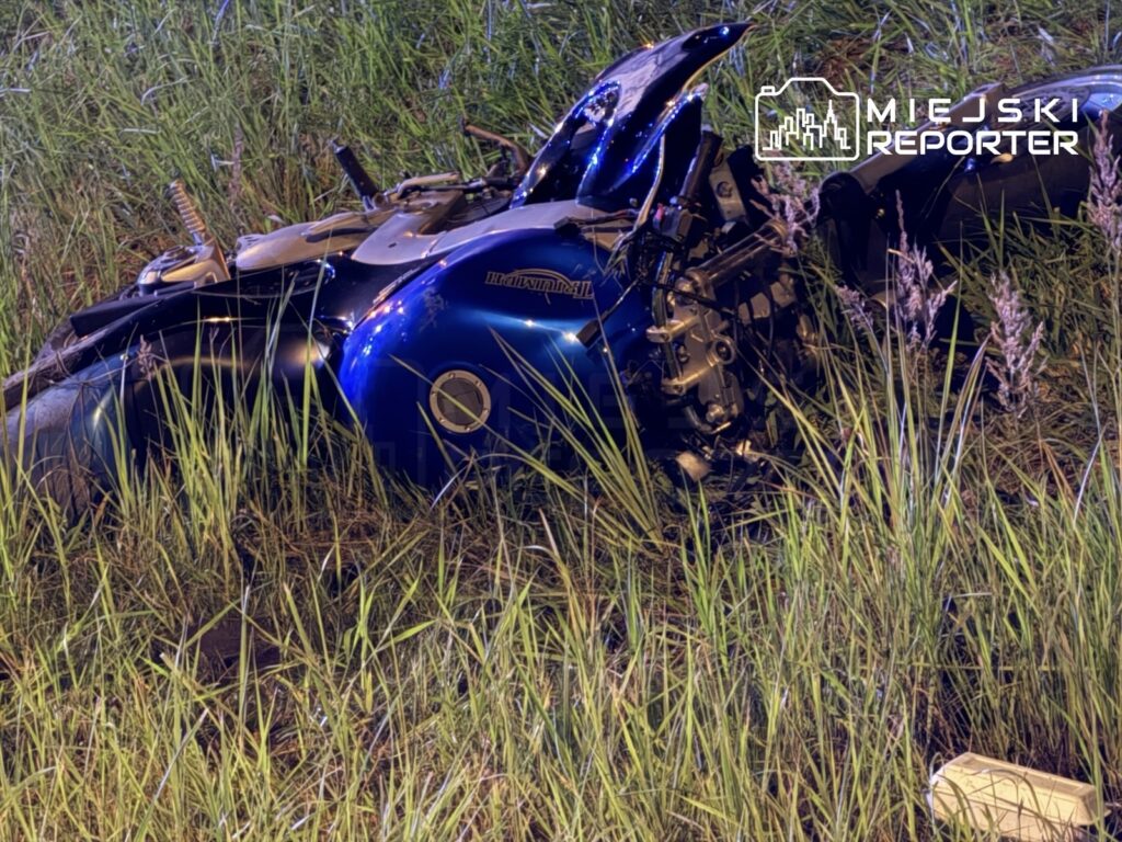 Zniszczony motocykl leży w wysokiej trawie obok drogi, z widocznymi uszkodzeniami silnika.