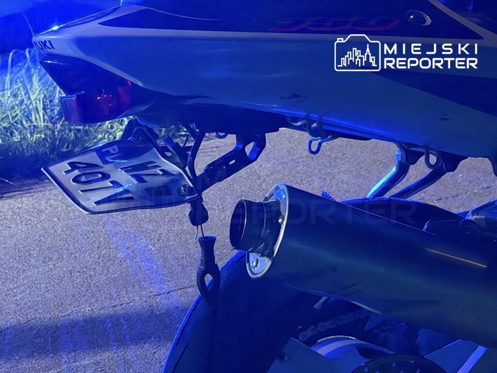 Motocykl z widoczną tablicą rejestracyjną i tłumikiem, oświetlony niebieskim światłem.