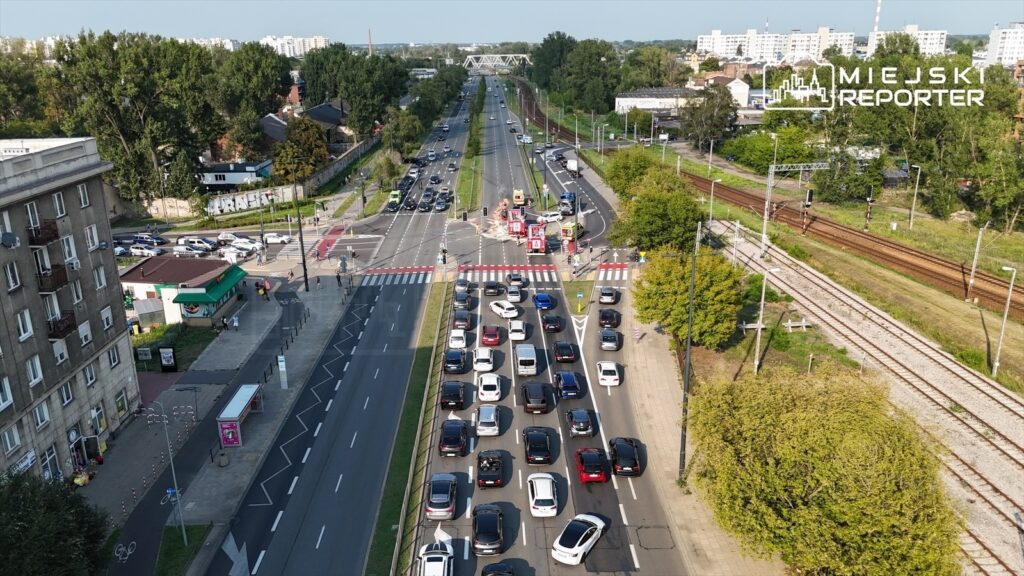 Ruch samochodowy na zatłoczonej ulicy z widocznymi pojazdami i sygnalizacją świetlną w tle.