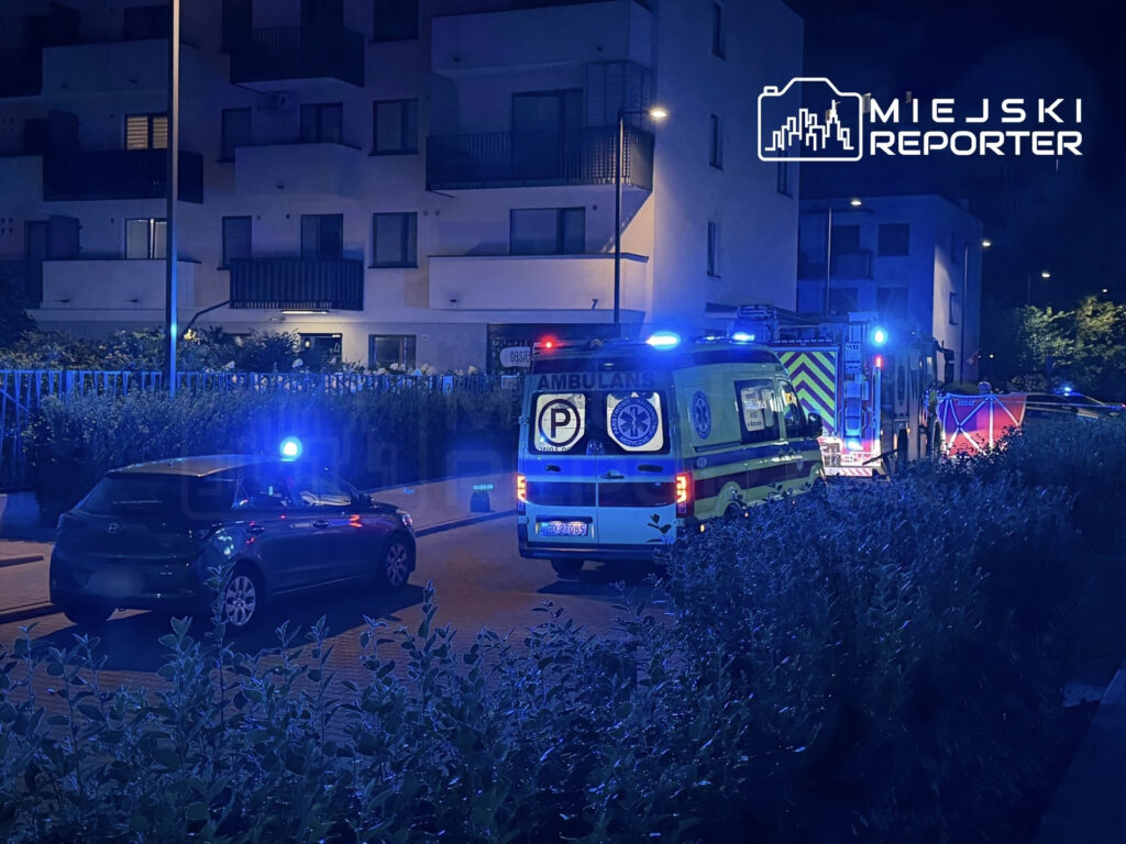 Ambulans i wóz strażacki z włączonymi sygnałami świetlnymi na ulicy w pobliżu nowoczesnych budynków mieszkalnych.