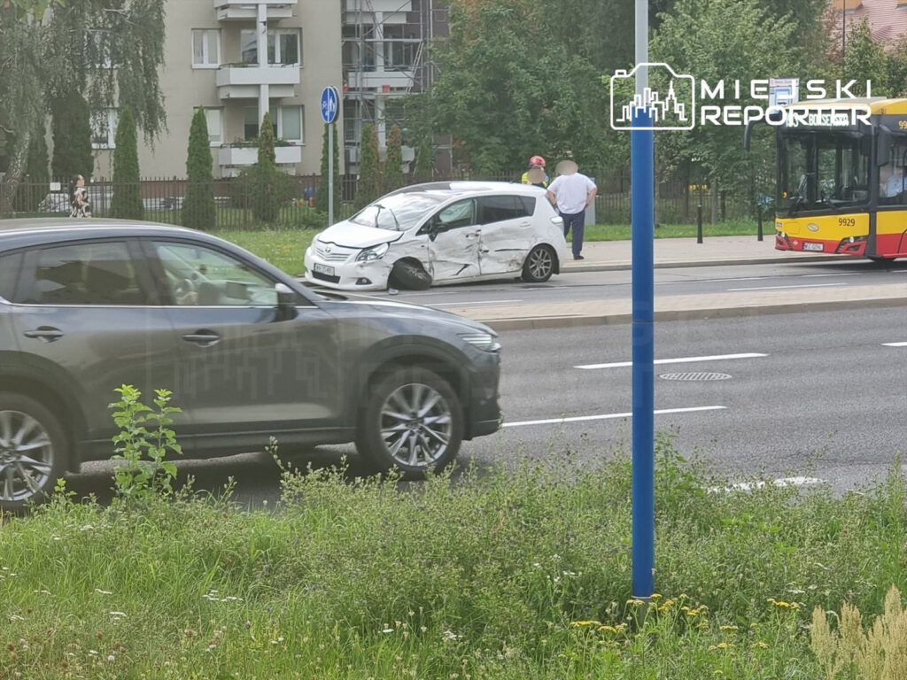 Zderzenie dwóch pojazdów na ulicy, z uszkodzonym białym autem i przejeżdżającym autobusem w tle, Mokotów.