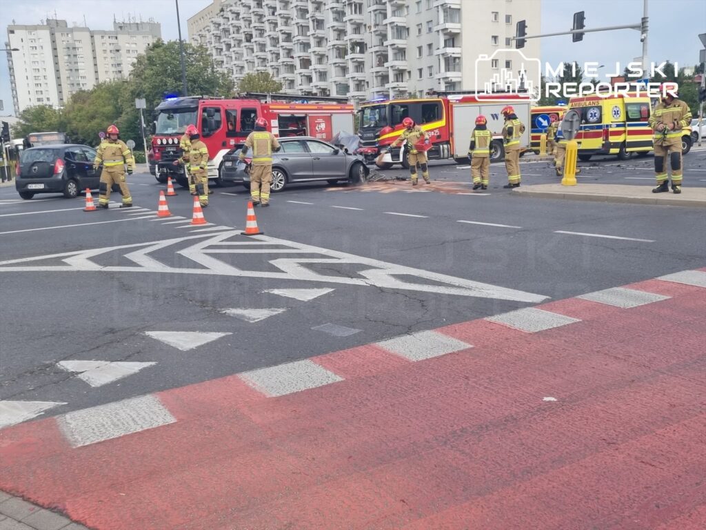 Strażacy zabezpieczają miejsce wypadku drogowego na Mokotowie, obok uszkodzonych samochodów i pojazdów ratunkowych.