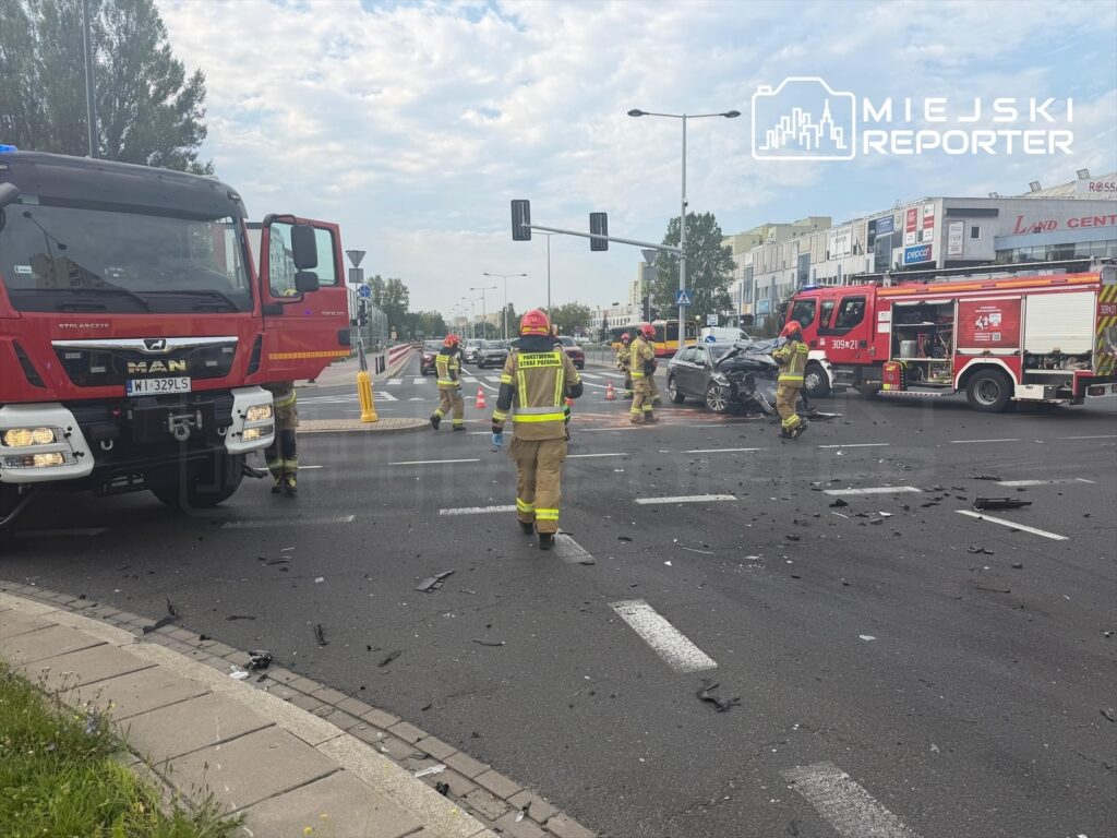 Strażacy pracują przy zderzeniu dwóch pojazdów na ruchliwej ulicy w Mokotowie, otoczeni przez wraki i fragmenty samochodów.