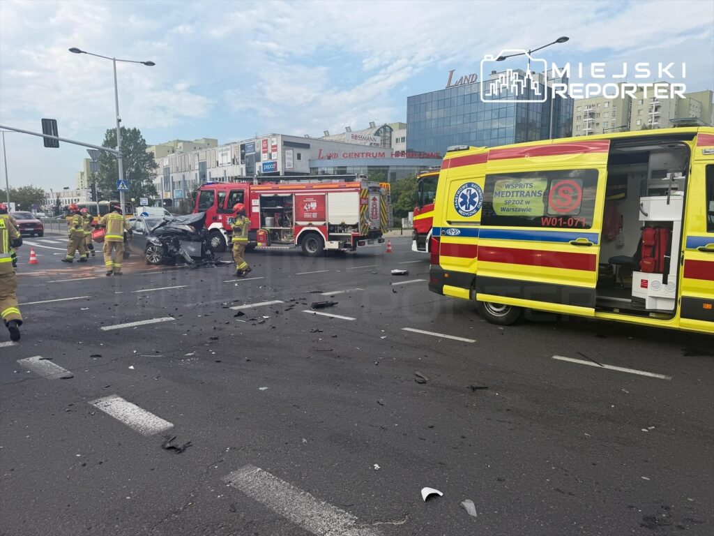 Strażacy usuwają skutki wypadku drogowego na Mokotowie, obok uszkodzonego samochodu i wozów ratunkowych.