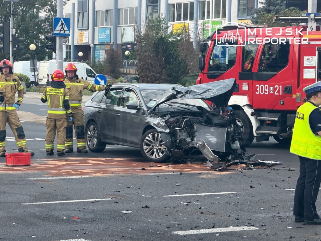 Strażacy w mundurach interweniują przy zderzeniu dwóch samochodów na ulicy w Mokotowie, obok uszkodzonego pojazdu.