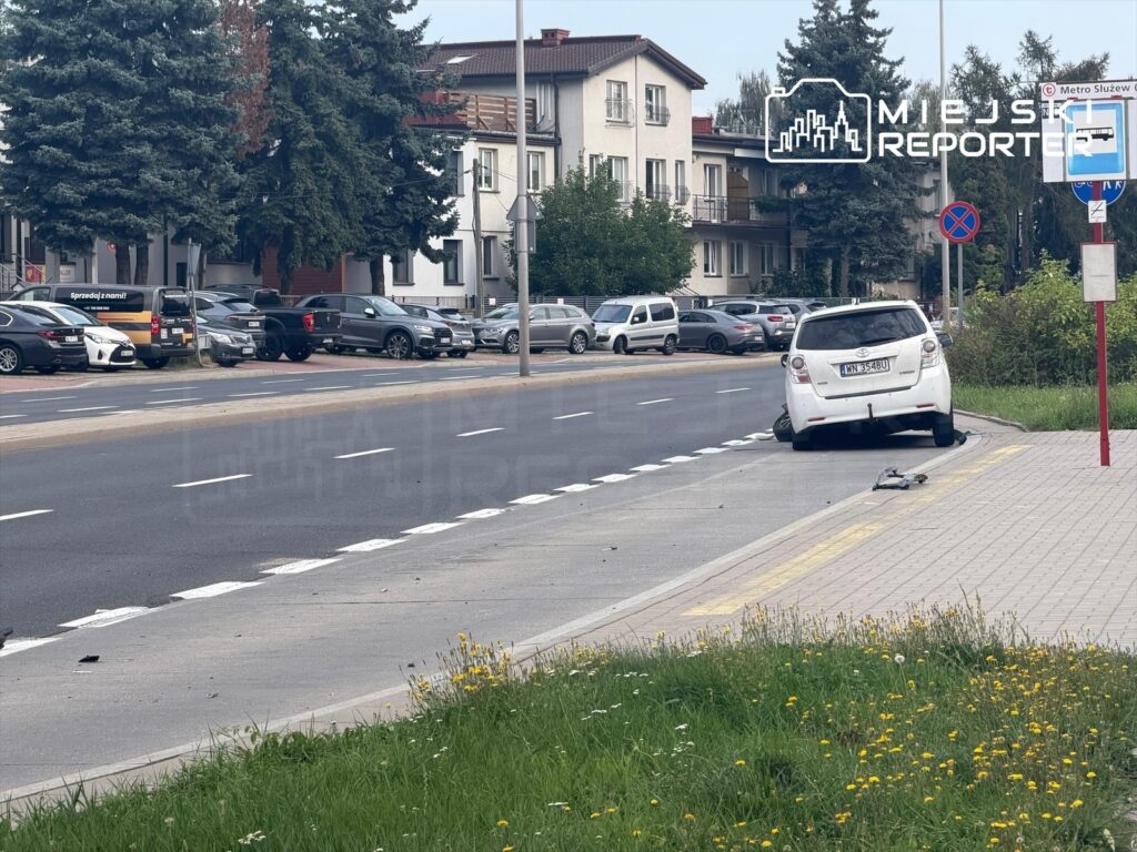 Biały samochód osobowy stoi na chodniku obok drogi, zwrócony w stronę ulicy, w tle widać zaparkowane pojazdy w Mokotowie.