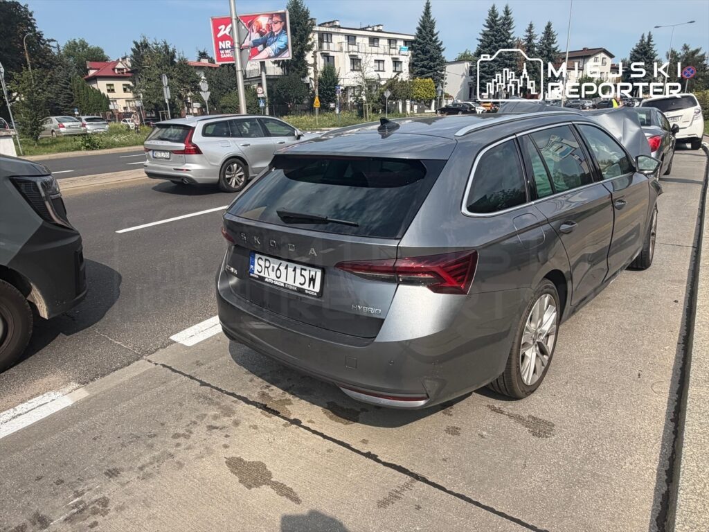 Szary samochód osobowy zaparkowany na ulicy w Mokotowie, obok innych pojazdów, w tle widoczne budynki i drzewa.