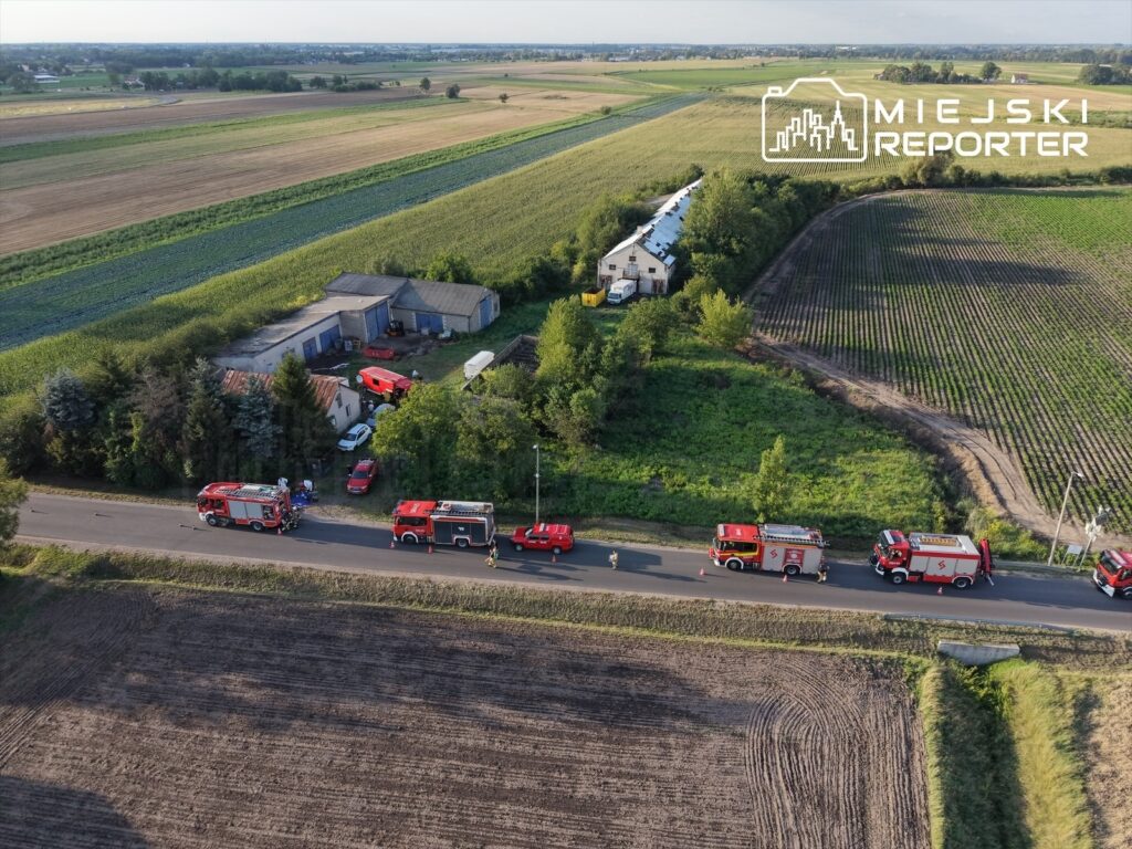 Wielka akcja ratunkowa z udziałem wozów strażackich na drodze obok niewielkiego budynku otoczonego zielenią.