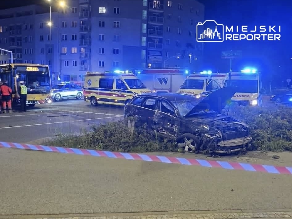 Uszkodzony samochód osobowy z otwartą maską stoi na trawie, obok zderzenia autobusu i karetki pogotowia.